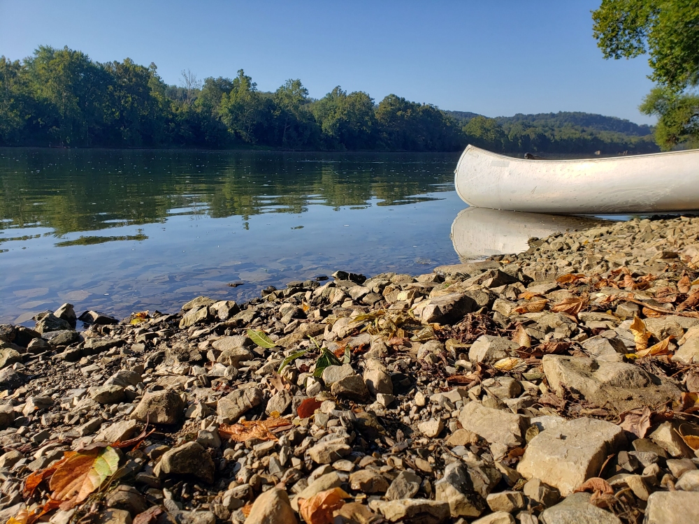 A canoe rests along the New River shoreline at the Whitethorne Boat Launch on a summer day.