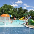 Guests use the splash features, slides, a water basketball goal, and sun bathing areas at the Frog Pond Swimming Pool on a sunny summer day.