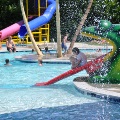 Water falls from a spray feature while a child slides down the Frog Slide at the Frog Pond Swimming Pool on a sunny summer day.